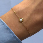 Bracelet fin en acier inoxydable doré avec une pierre naturelle de Jade Blanc ronde sertie sur un poignet.