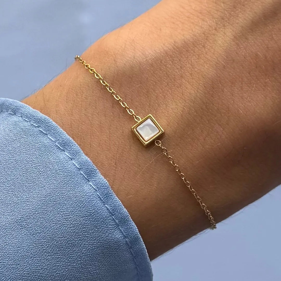 Bracelet fin en acier inoxydable doré, avec un carré en jade blanc, porté au poignet.