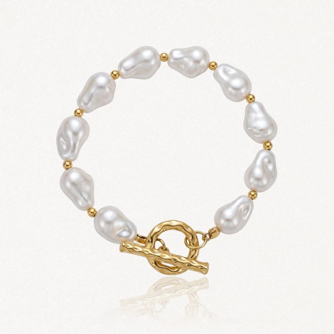 Bracelet en acier inoxydable doré avec de grandes perles baroques blanches et un fermoir toggle martelé.
