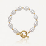 Bracelet en acier inoxydable doré avec de grandes perles baroques blanches et un fermoir toggle martelé.
