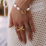 Bracelet en acier inoxydable doré, perles baroques blanches et fermoir toggle, porté par femme sur robe crochet.