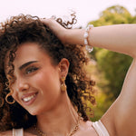 Bracelet en acier inoxydable perles baroques blanches, porté au poignet d'une femme souriante aux cheveux bouclés.