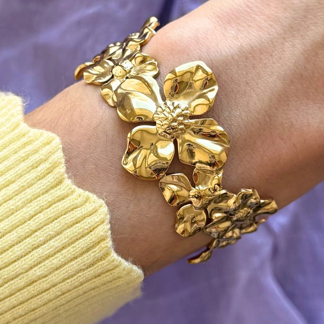 Bracelet en acier inoxydable doré brillant, orné de grandes fleurs sculpturales. Bijou floral chic porté au poignet.