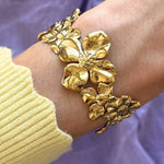 Bracelet en acier inoxydable doré brillant, orné de grandes fleurs sculpturales. Bijou floral chic porté au poignet.