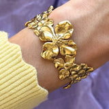 Bracelet en acier inoxydable doré brillant, orné de grandes fleurs sculpturales. Bijou floral chic porté au poignet.