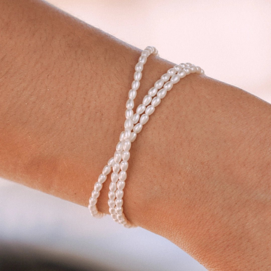 Bracelet en acier inoxydable de perles d'eau douce blanches torsadées sur un poignet.