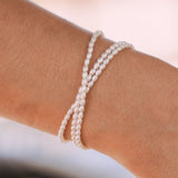 Bracelet en acier inoxydable de perles d'eau douce blanches torsadées sur un poignet.