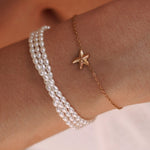 Bracelet acier inoxydable doré, étoile de mer pavée, et bracelet triple rang de perles fines sur poignet.