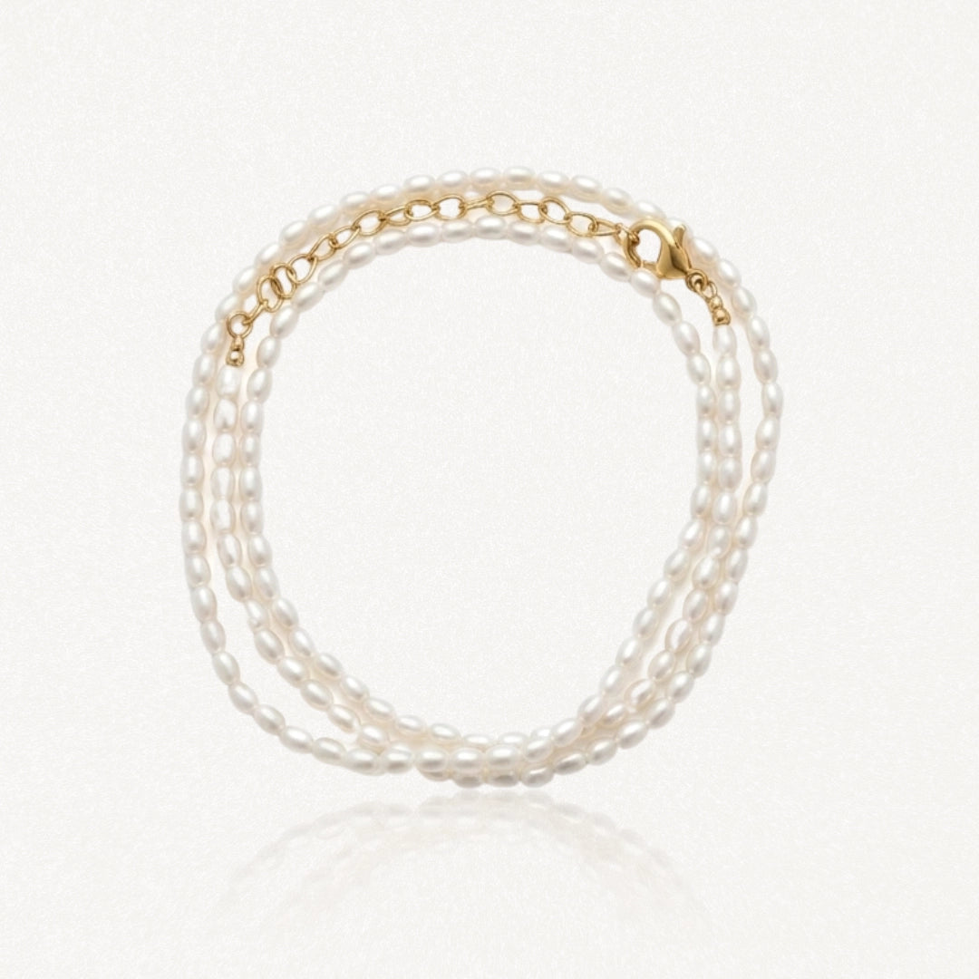 Bracelet à trois rangs de petites perles ovales blanches, avec fermoir et chaîne d'extension dorés.