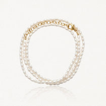 Bracelet à trois rangs de petites perles ovales blanches, avec fermoir et chaîne d'extension dorés.