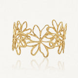 Bracelet jonc en acier inoxydable doré, avec un motif ajouré de fleurs dont la surface est texturée. Sur fond clair.