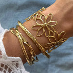 Main de femme portant 4 bracelets en acier inoxydable doré: un large jonc ajouré de fleurs et trois fins joncs martelés et