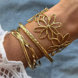 Main de femme portant 4 bracelets en acier inoxydable doré: un large jonc ajouré de fleurs et trois fins joncs martelés et