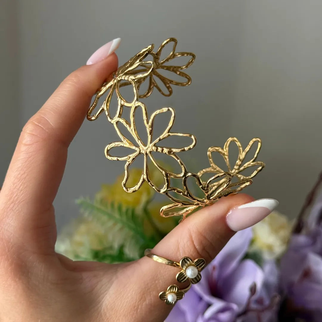 Bracelet jonc en acier inoxydable doré, ajouré de fleurs martelées. Une main tient le bracelet, portant une bague avec