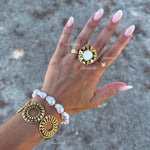 Bracelet manchette en acier inoxydable doré, avec deux motifs circulaires ornés de rayons.