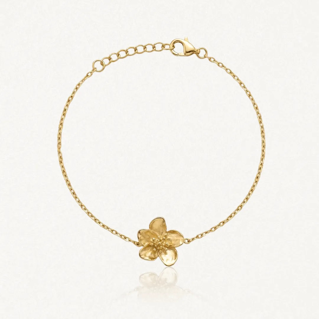 Bracelet fin en acier inoxydable doré, chaîne et pendentif fleur texturée, sur fond clair.