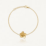 Bracelet fin en acier inoxydable doré, chaîne et pendentif fleur texturée, sur fond clair.