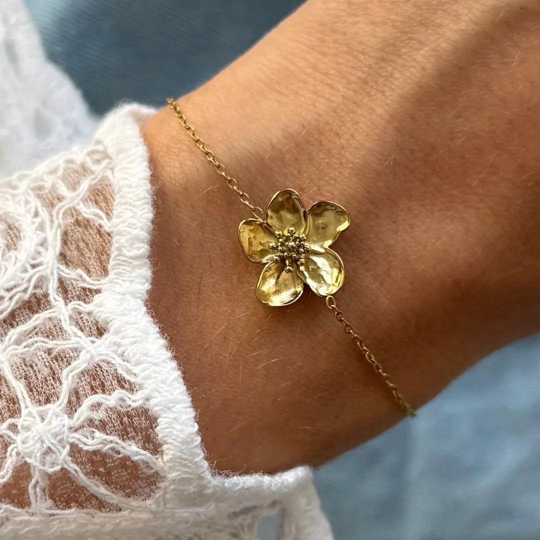 Bracelet fin en acier inoxydable doré, avec un pendentif fleur texturé à cinq pétales et cœur granuleux, porté sur un