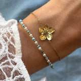 Bracelet en acier inoxydable doré avec pendentif fleur texturé, porté avec un second bracelet de perles et pierres naturelles