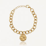 Bracelet doré à maillons ovales épais, avec un fermoir mousqueton et une breloque ronde texturée martelée.