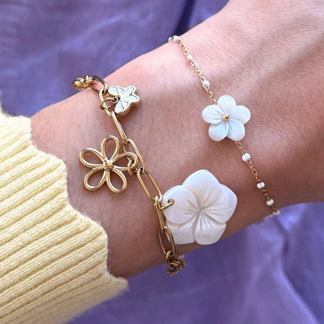 Deux bracelets en acier inoxydable doré. Un à maillons avec fleurs nacre et or ajourées, l'autre fin avec perles et fleur