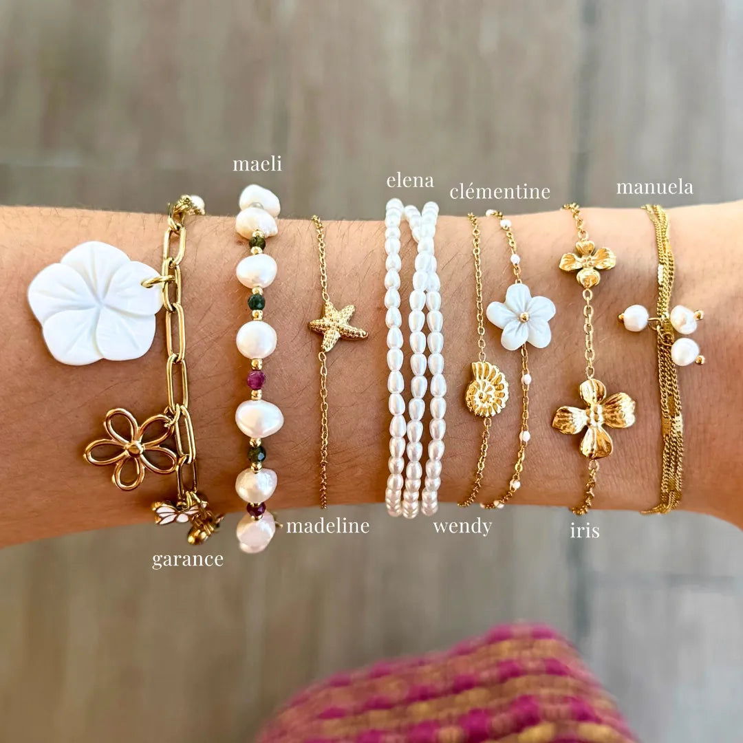 Bras portant 8 bracelets variés en acier inoxydable doré, nacre, perles et pierres naturelles. Motifs : fleurs, coquillage,
