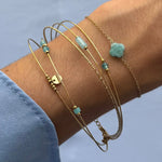 Bracelet multirangs en acier inoxydable doré orné de pierres naturelles bleu-vert variées et petites billes dorées, sur un