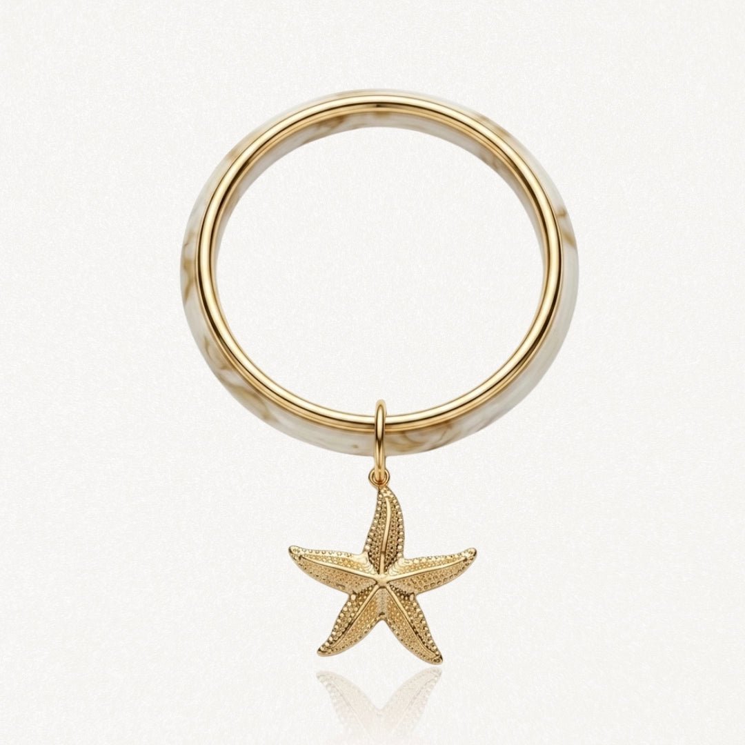 Bracelet jonc en acier inoxydable motif marbre blanc et doré avec pendentif étoile de mer dorée texturée.