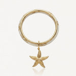 Bracelet jonc en acier inoxydable motif marbre blanc et doré avec pendentif étoile de mer dorée texturée.