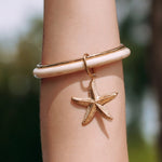 Bracelet jonc en acier inoxydable doré avec partie beige marbrée et charm étoile de mer texturée, sur un bras.