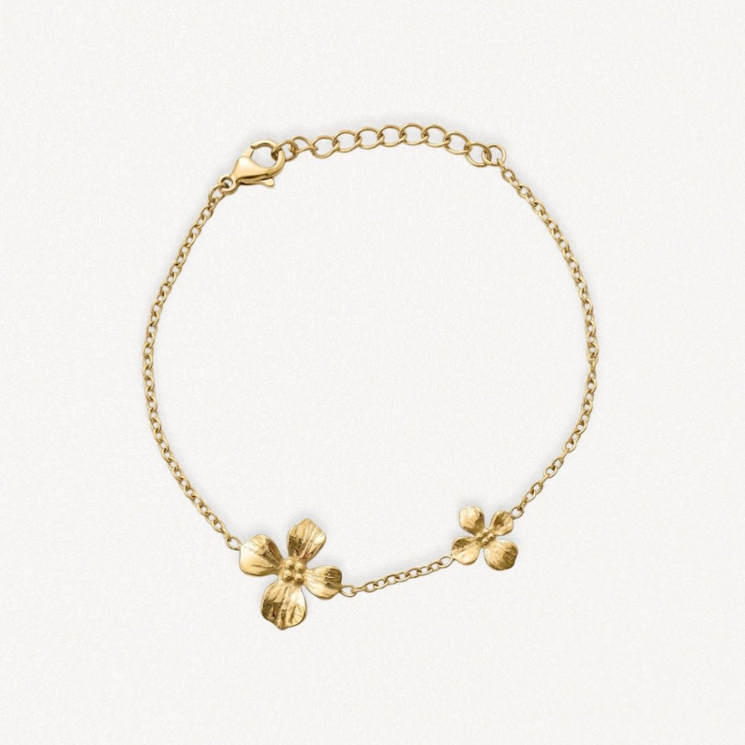 Bracelet en acier inoxydable couleur or avec deux charmes fleurs délicates, chaîne fine et fermoir mousqueton.