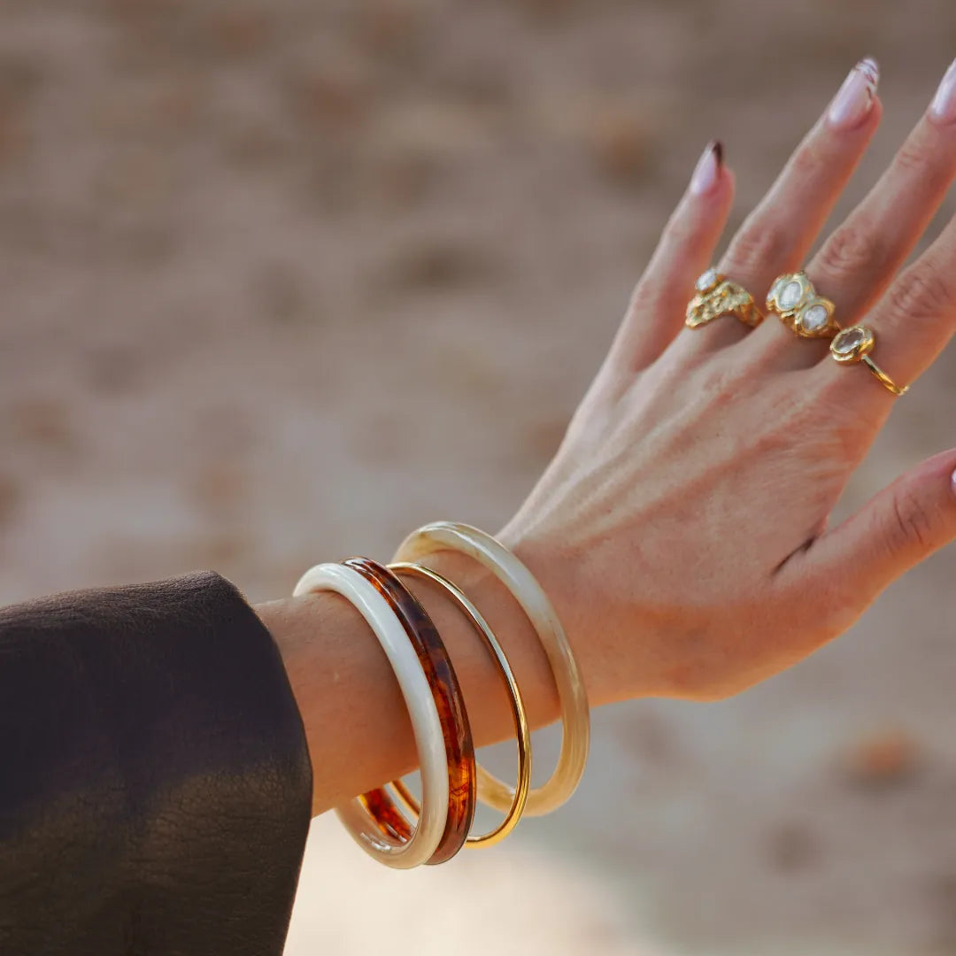 Bracelet Johanna en acier inoxydable doré porté au poignet avec d'autres joncs en résine blanche et écaille