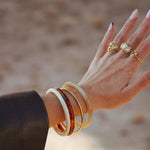 Bracelet Johanna en acier inoxydable doré porté au poignet avec d'autres joncs en résine blanche et écaille