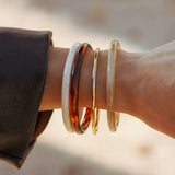 Bracelet Johanna en acier inoxydable doré porté au poignet avec trois autres joncs en résine de différentes couleurs