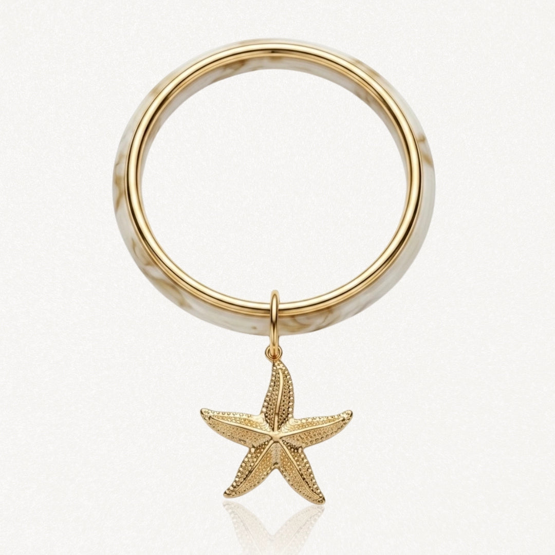 Bracelet jonc marbré crème et or avec un pendentif étoile de mer dorée texturée.