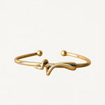 Bracelet jonc rigide ouvert en métal doré avec motif nœud central asymétrique et extrémités boules sur fond blanc.