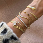 Poignet portant 5 bracelets en acier inoxydable doré : jonc serpent à têtes, chaîne avec pierres naturelles et 3 bracelets