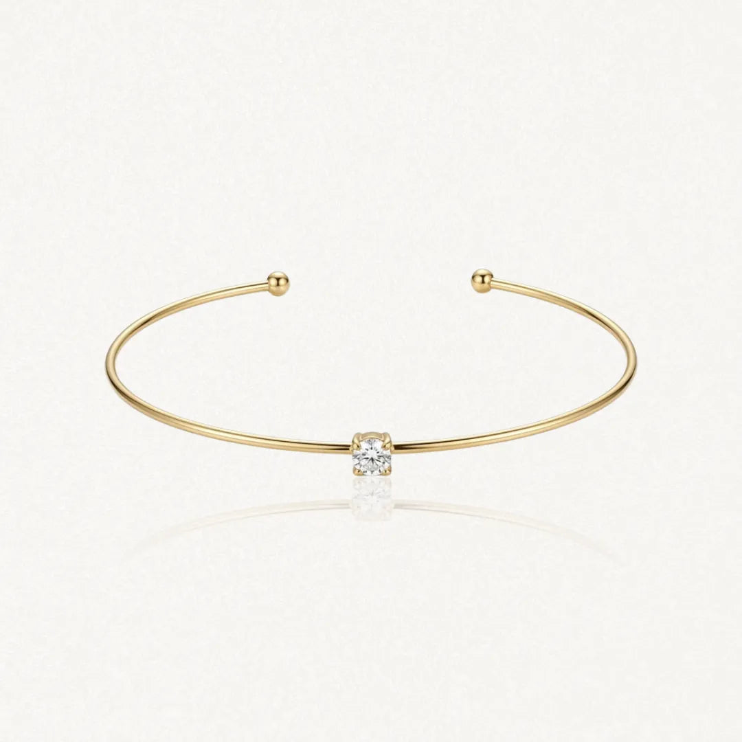 Bracelet jonc fin ouvert en acier inoxydable doré avec un zirconium carré central et deux boules aux extrémités.