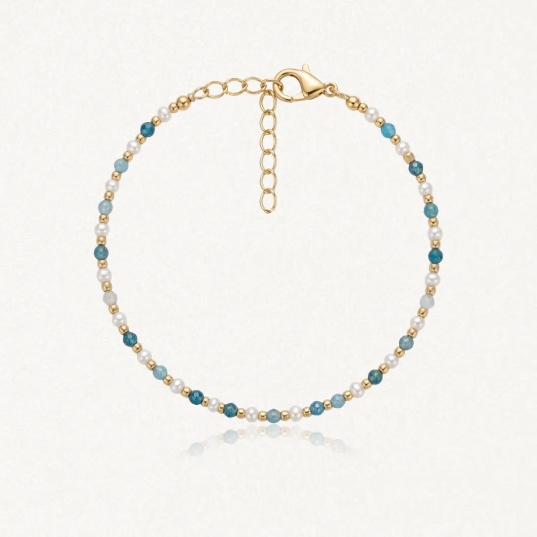 Bracelet en acier inoxydable doré, perles blanches et apatite facettée bleue. Fermoir mousqueton et chaînette d'extension.