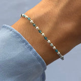 Bracelet d'apatite bleues-vertes, perles blanches et billes d'acier inoxydable doré sur un poignet avec une manche bleue.