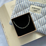 Bracelet acier inoxydable doré, perles blanches et apatite bleue, présenté dans sa boîte, près d'un livre et d'une pochette