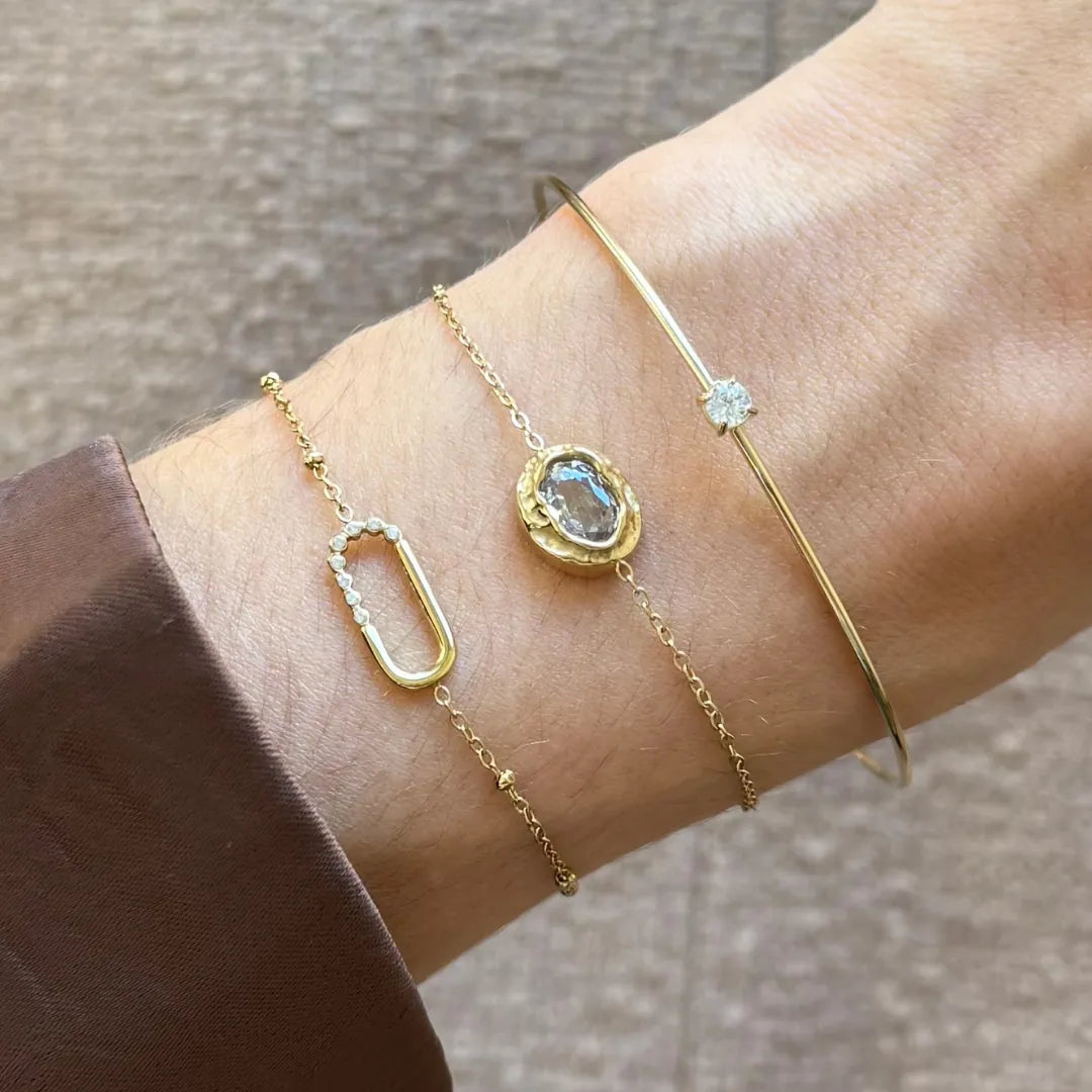 Bracelet Kendall en acier inoxydable doré avec strass en zirconium porté au poignet avec d'autres bracelets