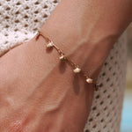 Bracelet fin en acier inoxydable doré, orné de multiples petites coquilles, porté au poignet.