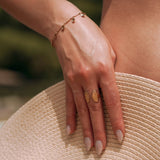 Bracelet femme acier inoxydable doré, chaîne fine avec breloques scintillantes, porté au poignet, main sur un chapeau de