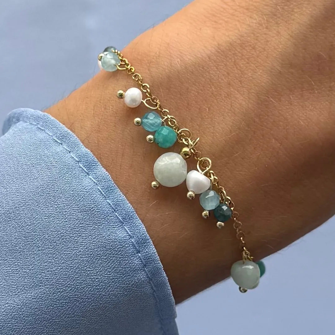 Bracelet en acier inoxydable doré sur un poignet, avec des breloques rondes et cœur en amazonite bleu-vert et perles d'eau