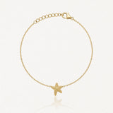 Bracelet doré fin avec une étoile de mer texturée au centre, fermoir mousqueton et chaîne d'extension.