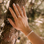 Bracelet femme en acier inoxydable composé de perles blanches et d'une étoile de mer dorée, posé sur un arbre.
