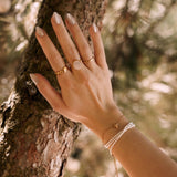 Bracelet femme en acier inoxydable composé de perles blanches et d'une étoile de mer dorée, posé sur un arbre.