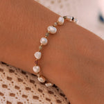Bracelet en acier inoxydable avec perles baroques blanches, petites perles dorées et perles gemmes colorées porté au poignet.