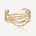 Bracelet manchette doré, ajouré, avec un motif organique irrégulier composé de formes ondulées et entrelacées.